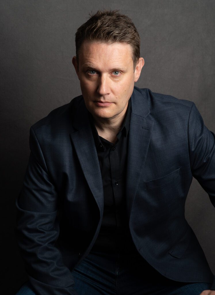 A man dressed in a dark blue suite looking straight into the camera.