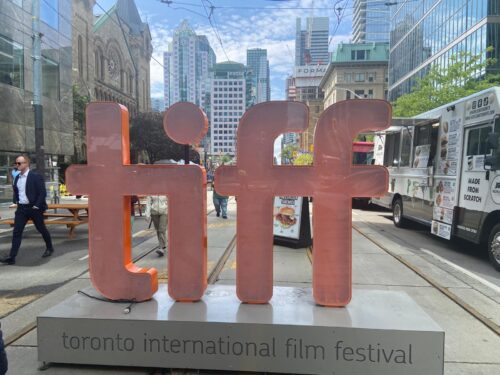 Oversized “tiff” letters displayed on a city street during the Toronto International Film Festival, with buildings and food trucks nearby.